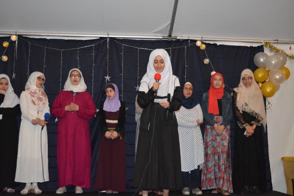 Al Huda Society student program presentation with girls speaking on stage
